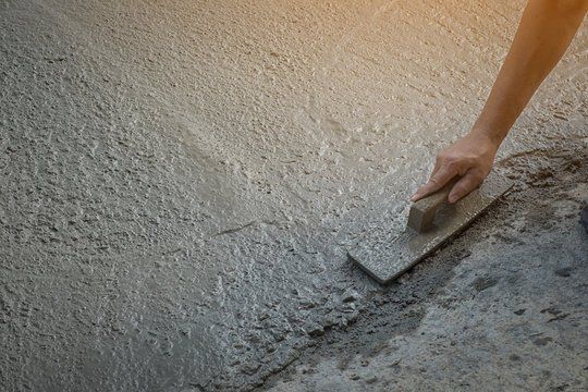 Person smoothing wet concrete with a trowel, creating a flat surface.