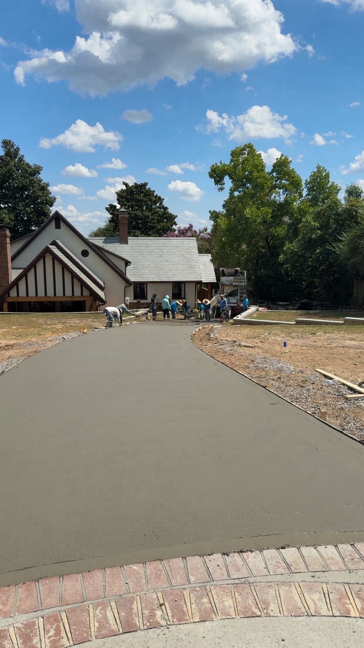 Newly poured concrete driveway leading to a house under construction; workers in the background.
