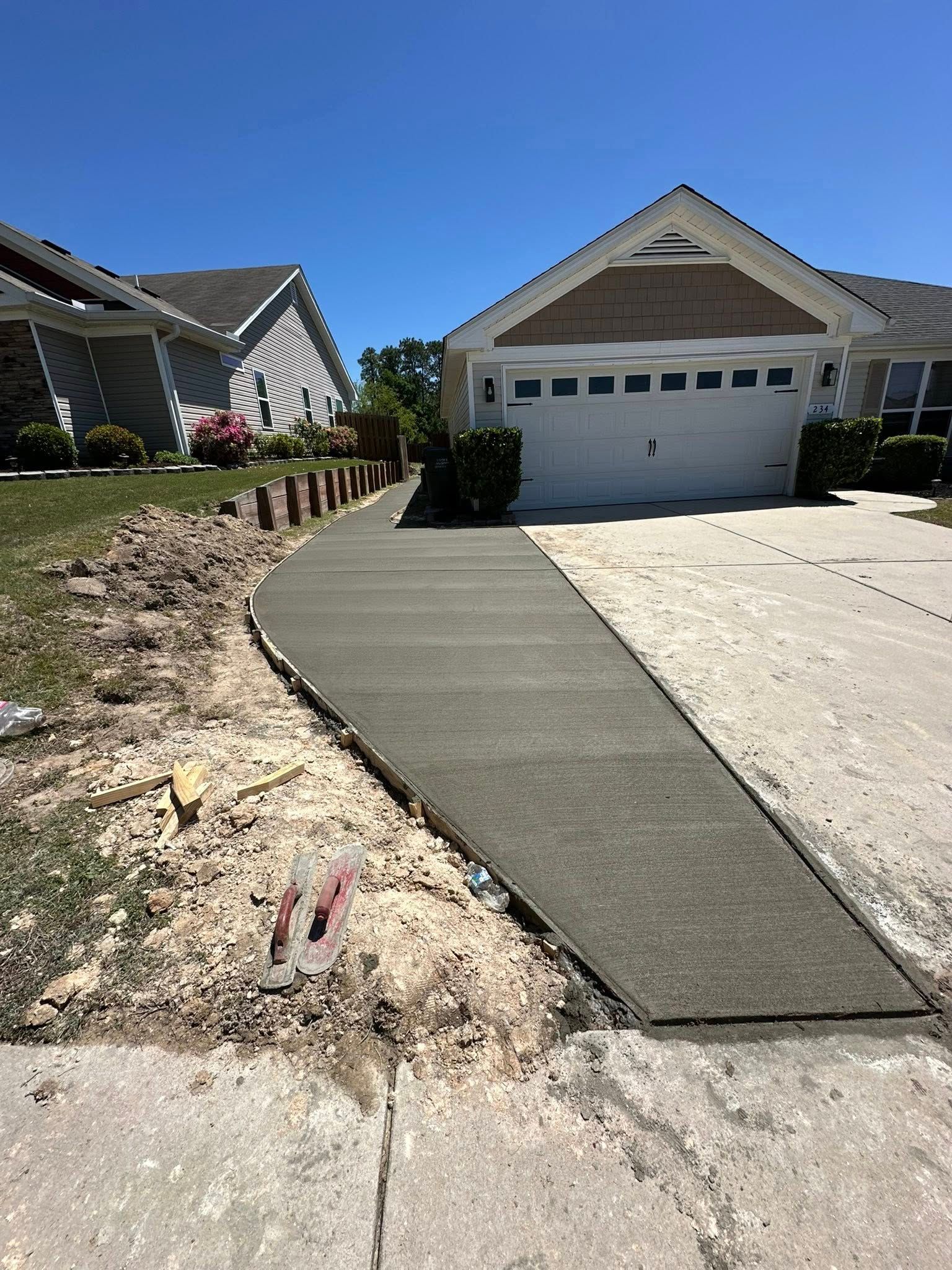 New concrete walkway curves from street to house with white garage door. Blue sky.