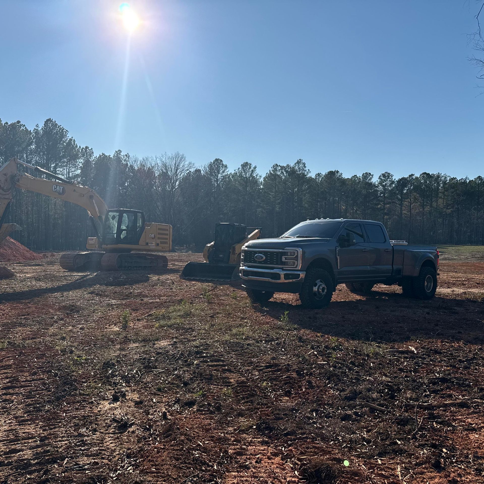 Construction site with a truck and excavator under a bright sun.
