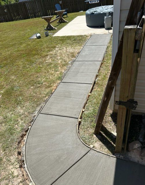 A newly poured concrete pathway curves through a grassy backyard.