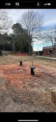 Two pipes in a brown, dirt area with trees and a building in the background. Overcast sky.