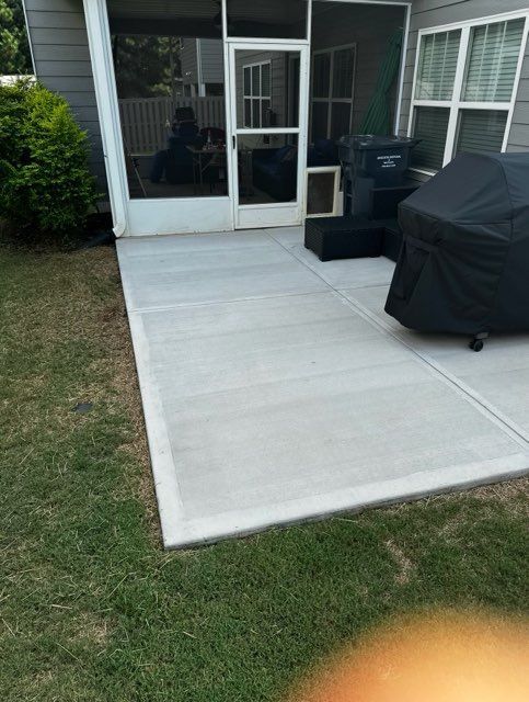 Concrete patio adjacent to a screened porch and grass yard. A grill is covered.