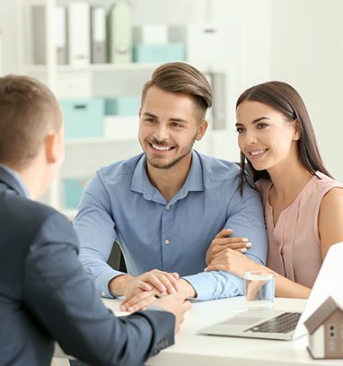 Smiling couple meeting with an advisor at a desk in a bright office, shaking hands over a laptop