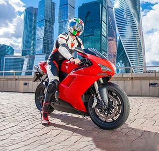 Motorcyclist in racing gear on a red sport bike with city skyscrapers in the background