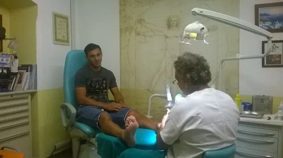 Visita odontoiatrica con il paziente reclinato sulla poltrona mentre il dentista lo esamina sotto una luce intensa dall’alto