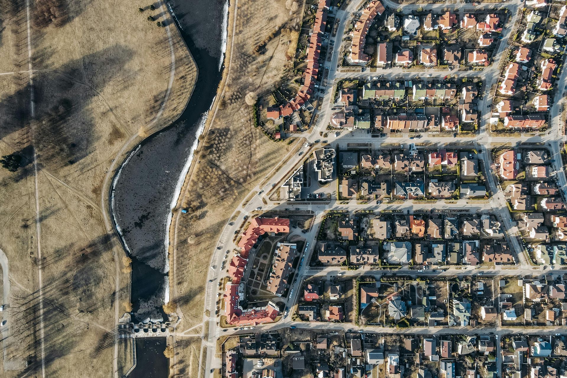 Aerial view of a suburban neighborhood beside a winding river and dry grassy land.