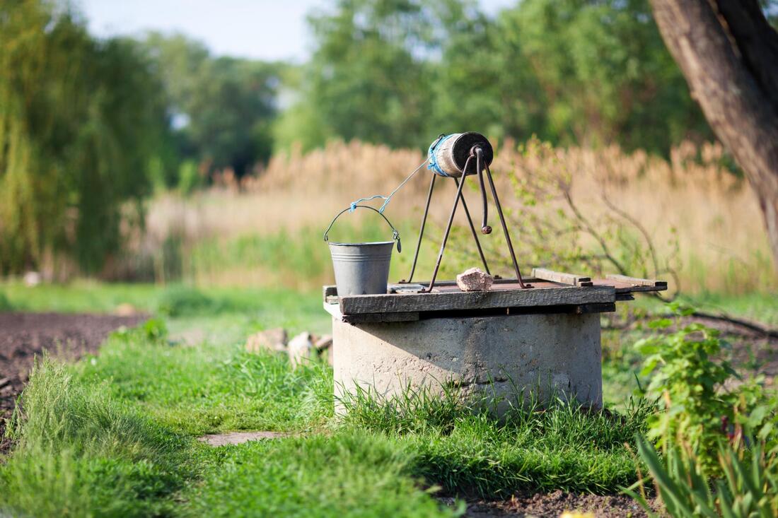 Old well in a grassy garden path with a metal tripod and bucket