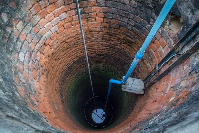 Looking down a brick-lined well with ropes and a metal ladder descending into darkness