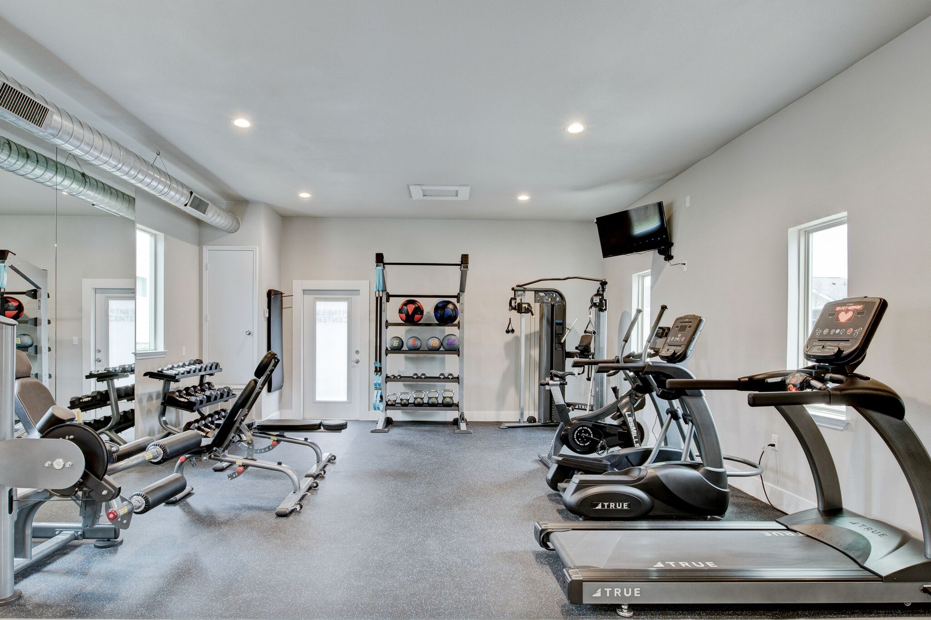 A gym with a treadmill, exercise bike, dumbbells, and a mirror.