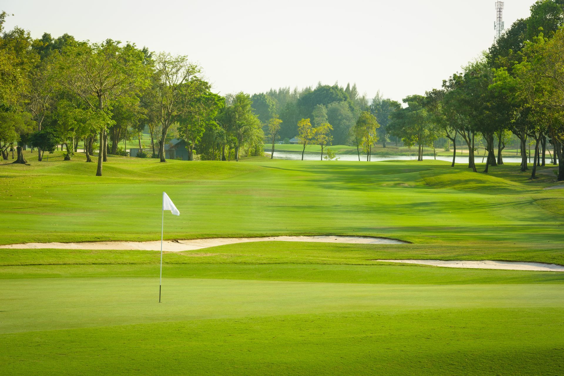 A golf course with a white flag on the green.