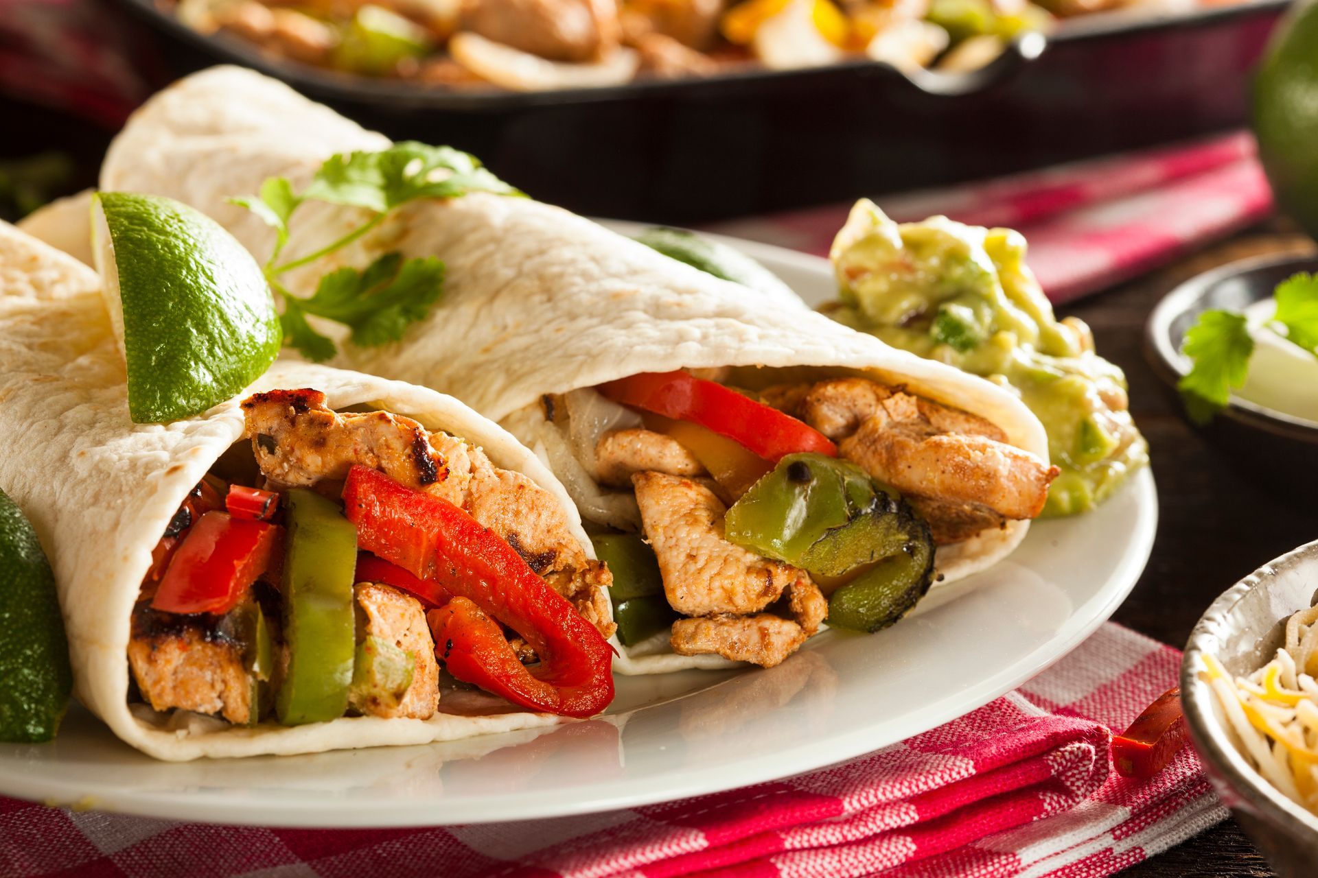 A burrito with chicken , peppers , and guacamole on a white plate.