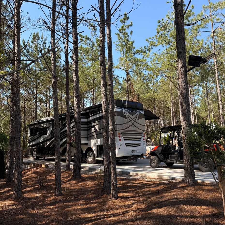 Large RV parked on a concrete pad in a wooded area, awning extended.