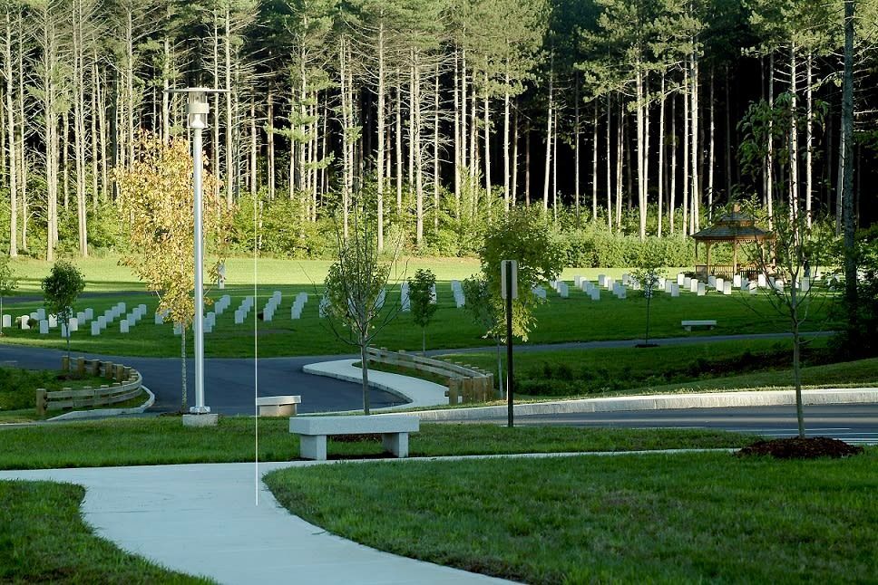 A park with graves in a grassy area, a winding path, trees in the background.