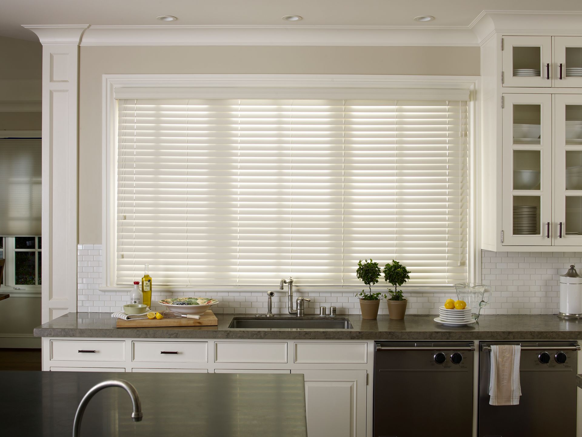 Kitchen with light wood blinds over the sink, white cabinets, and dark countertop.