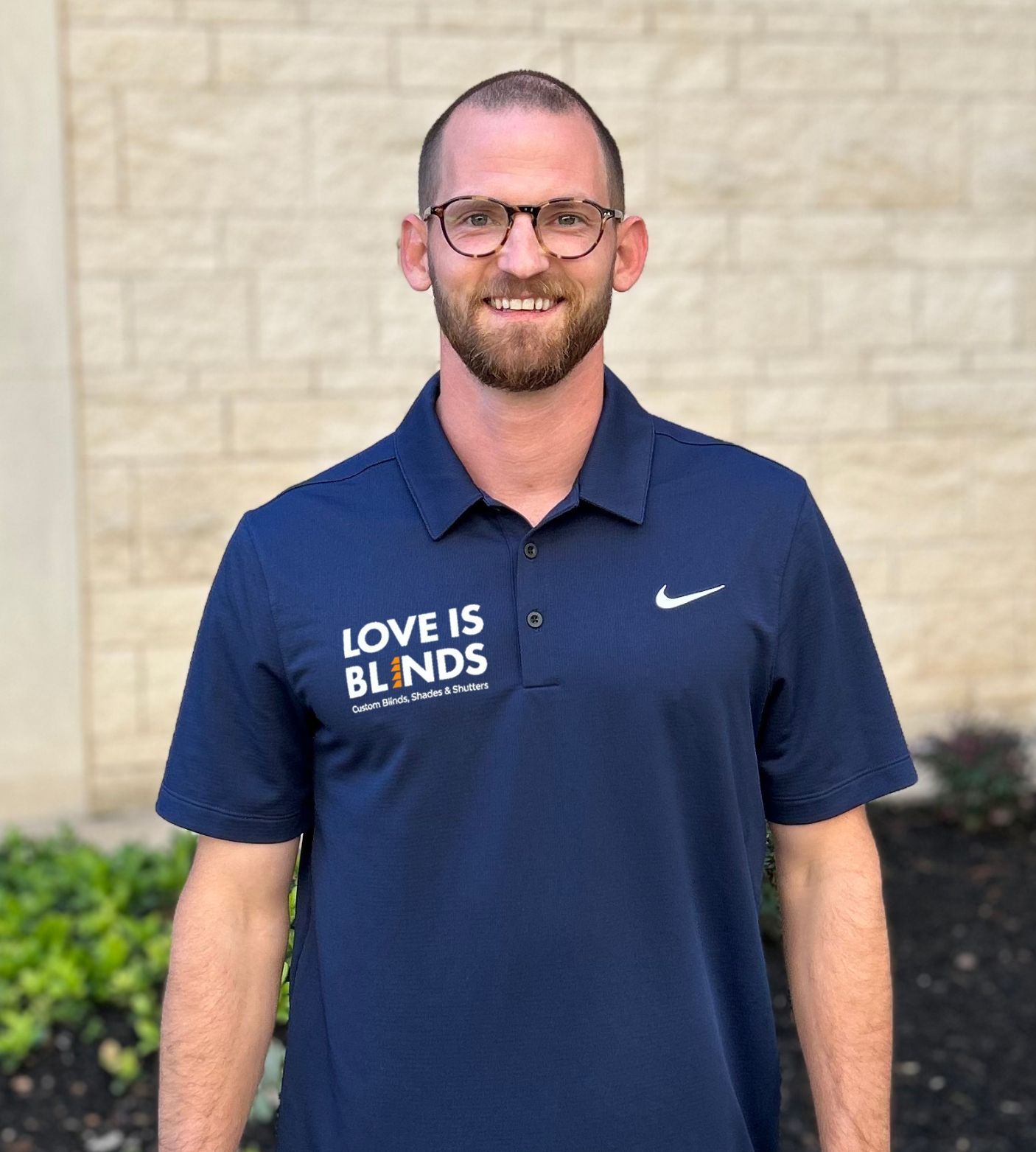 Man in blue polo with Nike logo, "Love is Blinds" text, standing outside. He wears glasses and smiles.