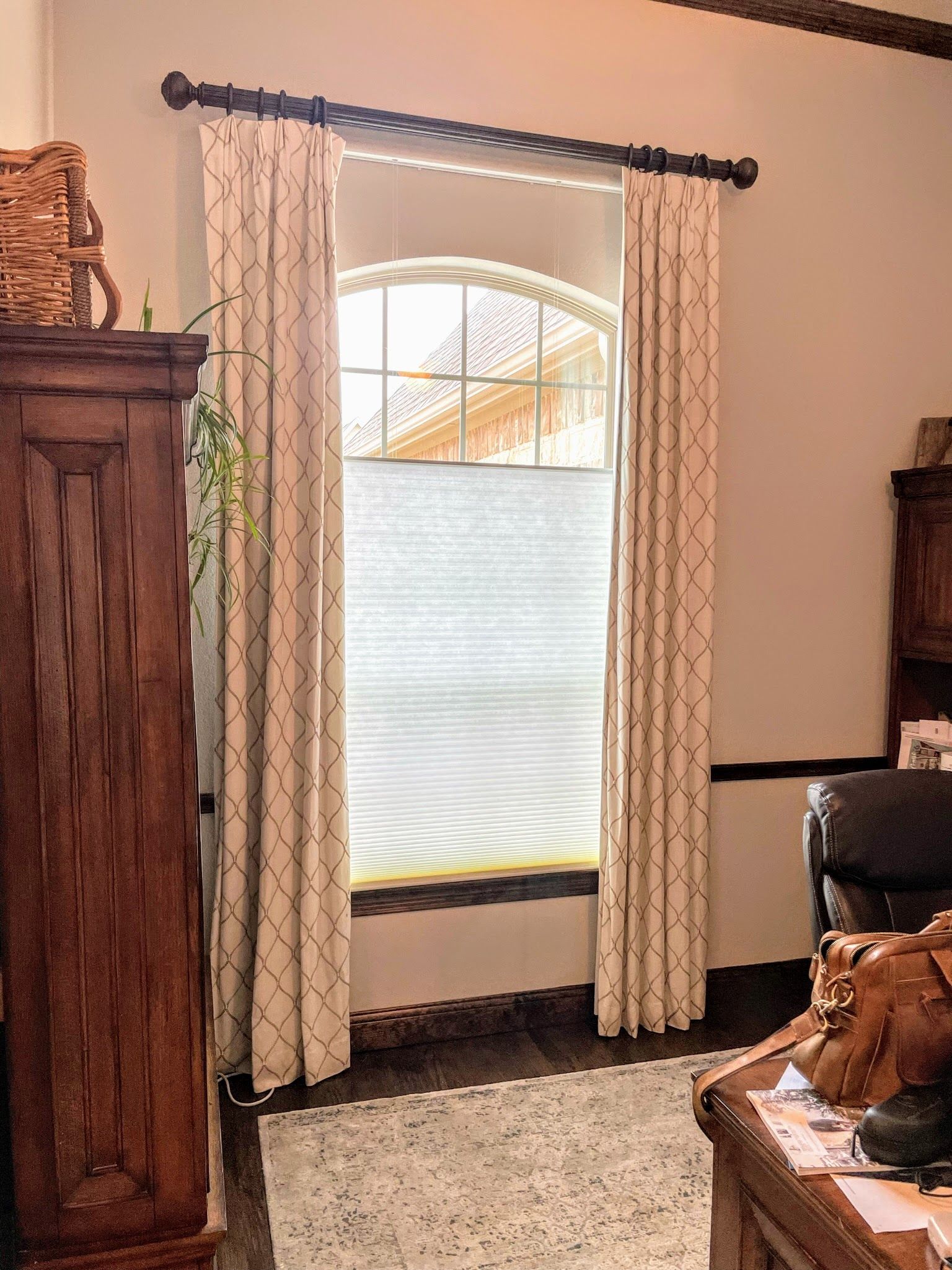 Window with arched top, framed by patterned curtains and a dark wooden rod, with a partially visible cellular shade.