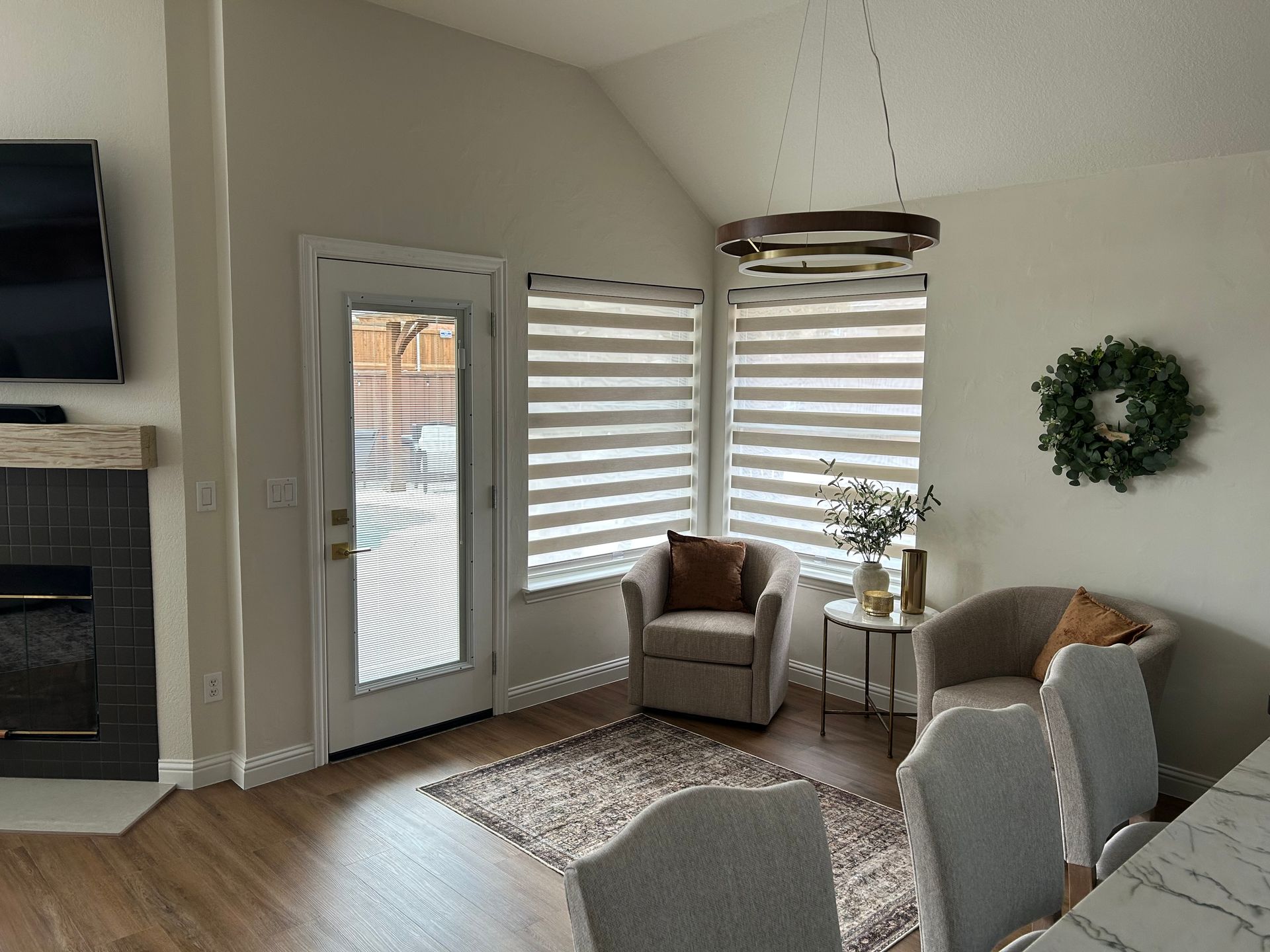 Living room with fireplace, door, windows with blinds, two armchairs, rug, and pendant light.