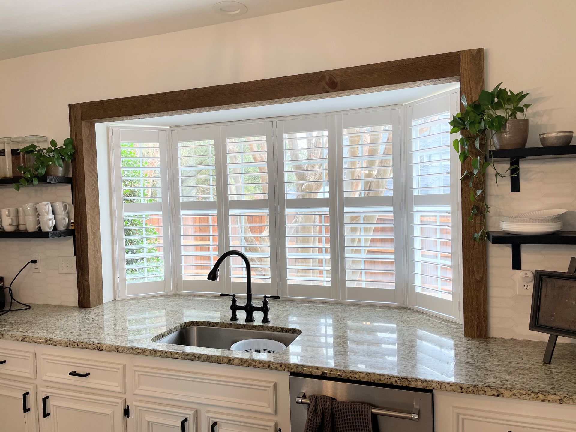 Kitchen with bay window, granite countertop, stainless steel sink, white shutters, and rustic wood trim.