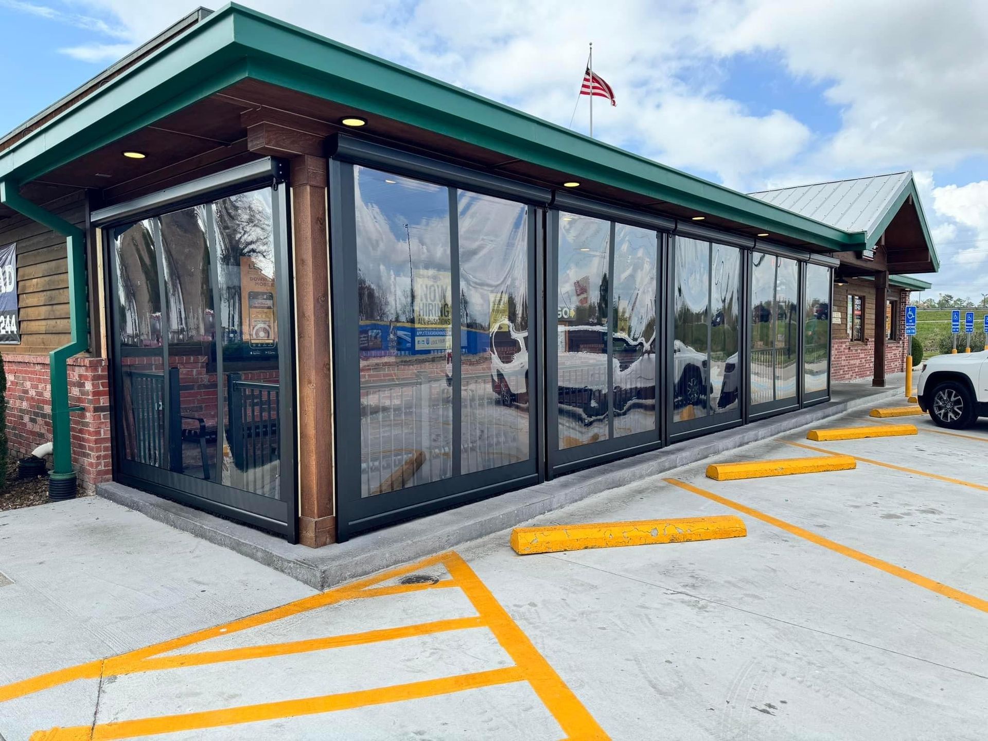 Enclosed outdoor dining area with clear vinyl panels, brick and wood accents, and parking in front.
