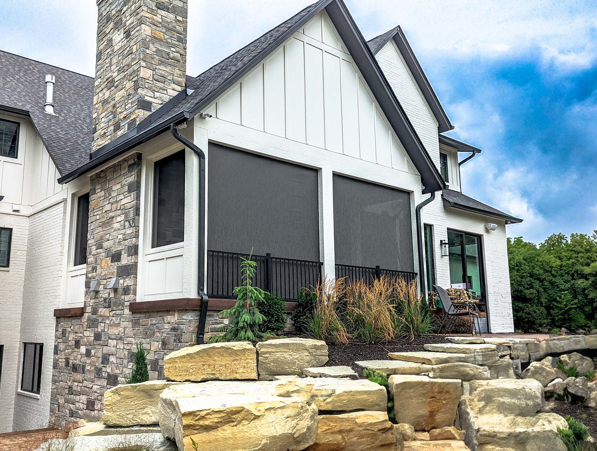 White house with stone accents and retractable shades on a patio. Large rocks in the foreground.