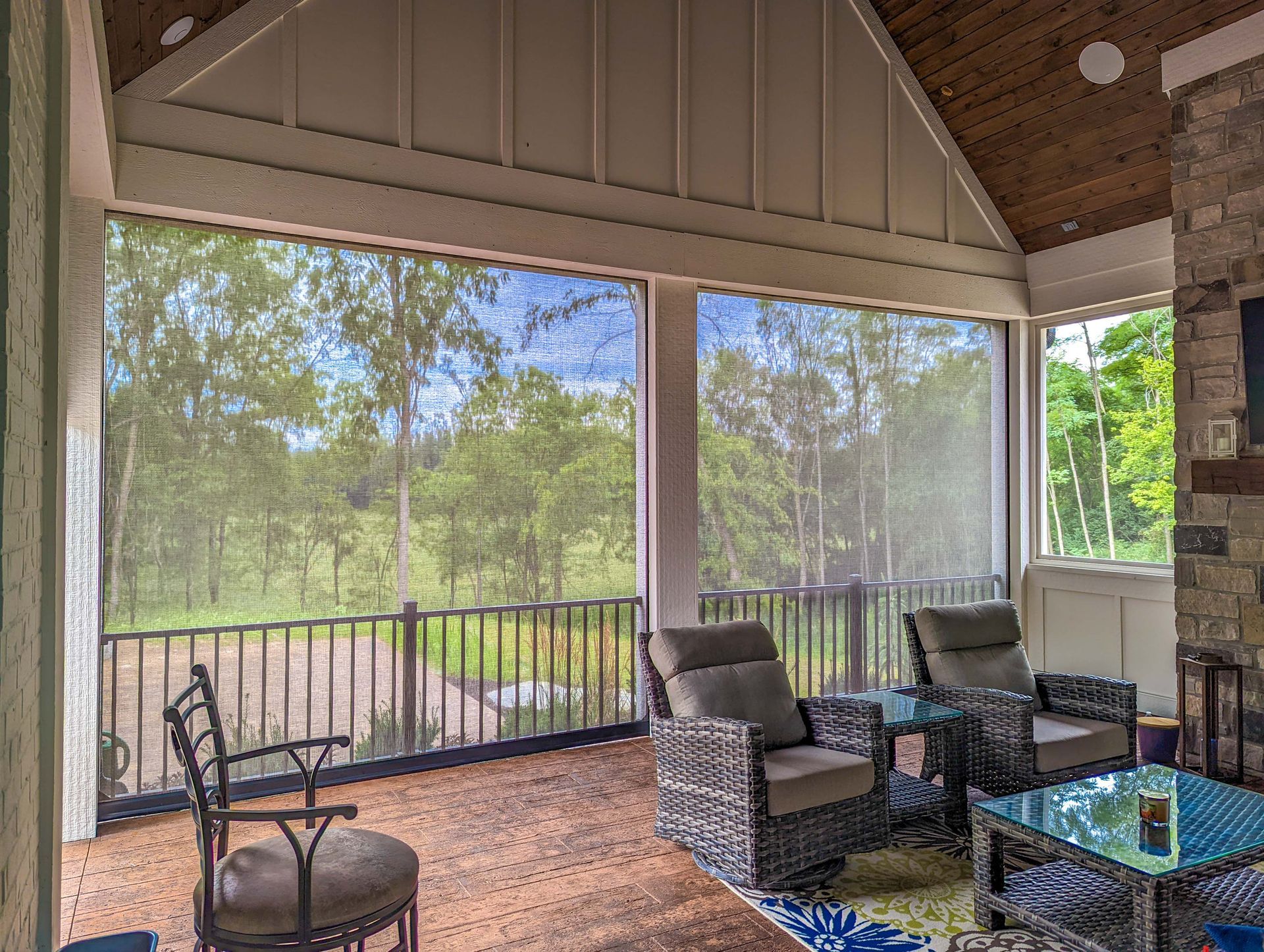 Screened porch with outdoor seating and view of trees.