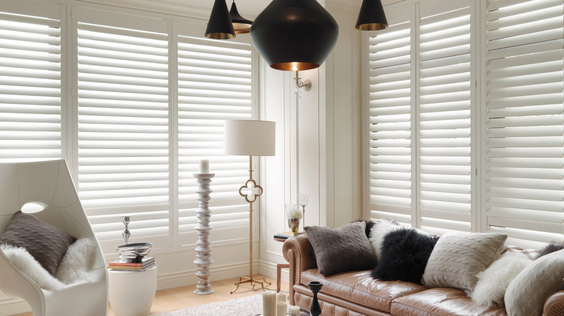 Living room with white shutters, leather couch, and decorative pillows.