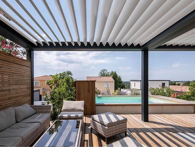 Outdoor patio with a louvred roof, seating, and a pool in the background.