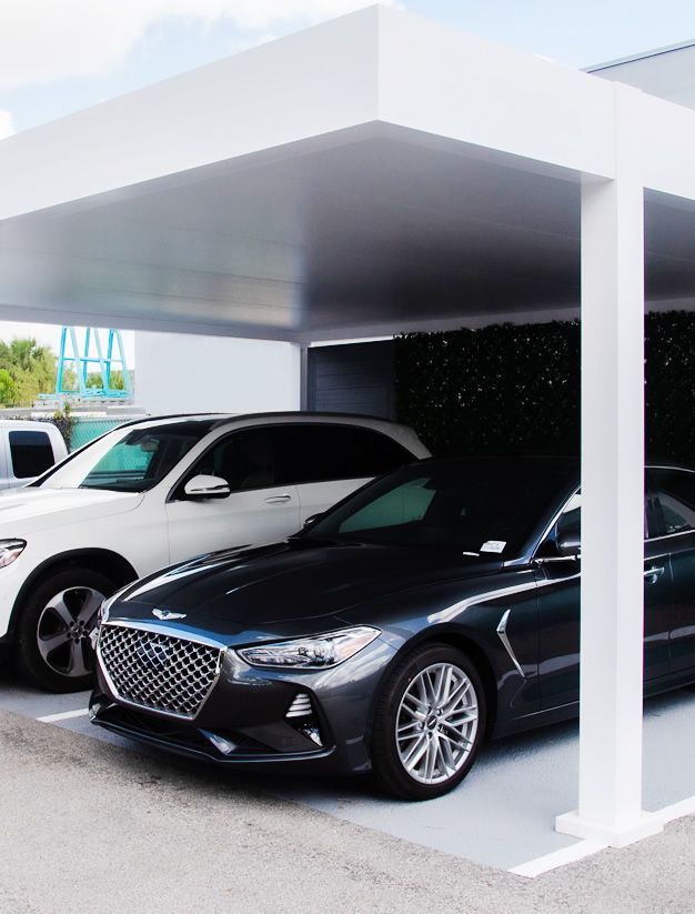 Two cars are parked under a canopy in a parking lot