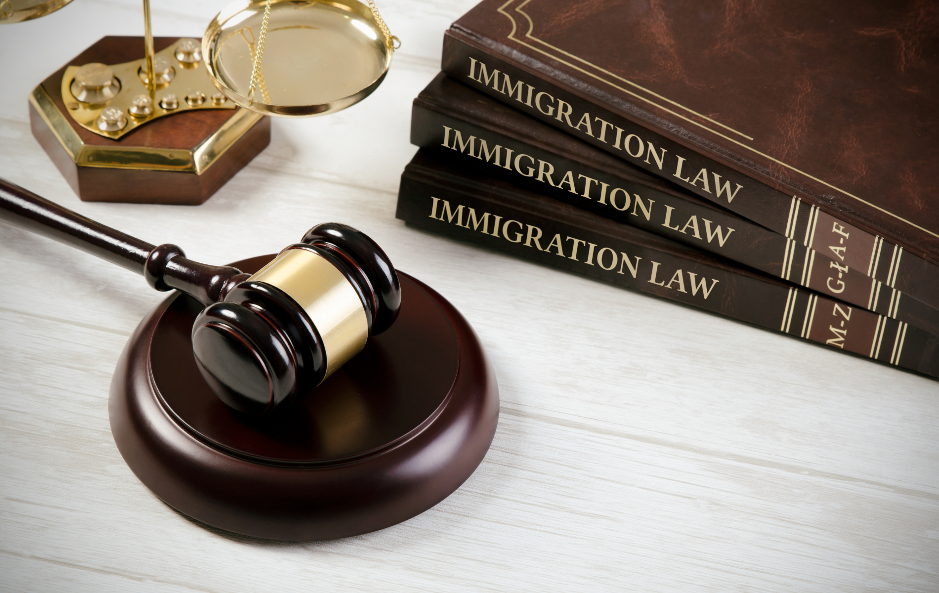 Gavel on block, balance scale, and stacked immigration law books on a table.