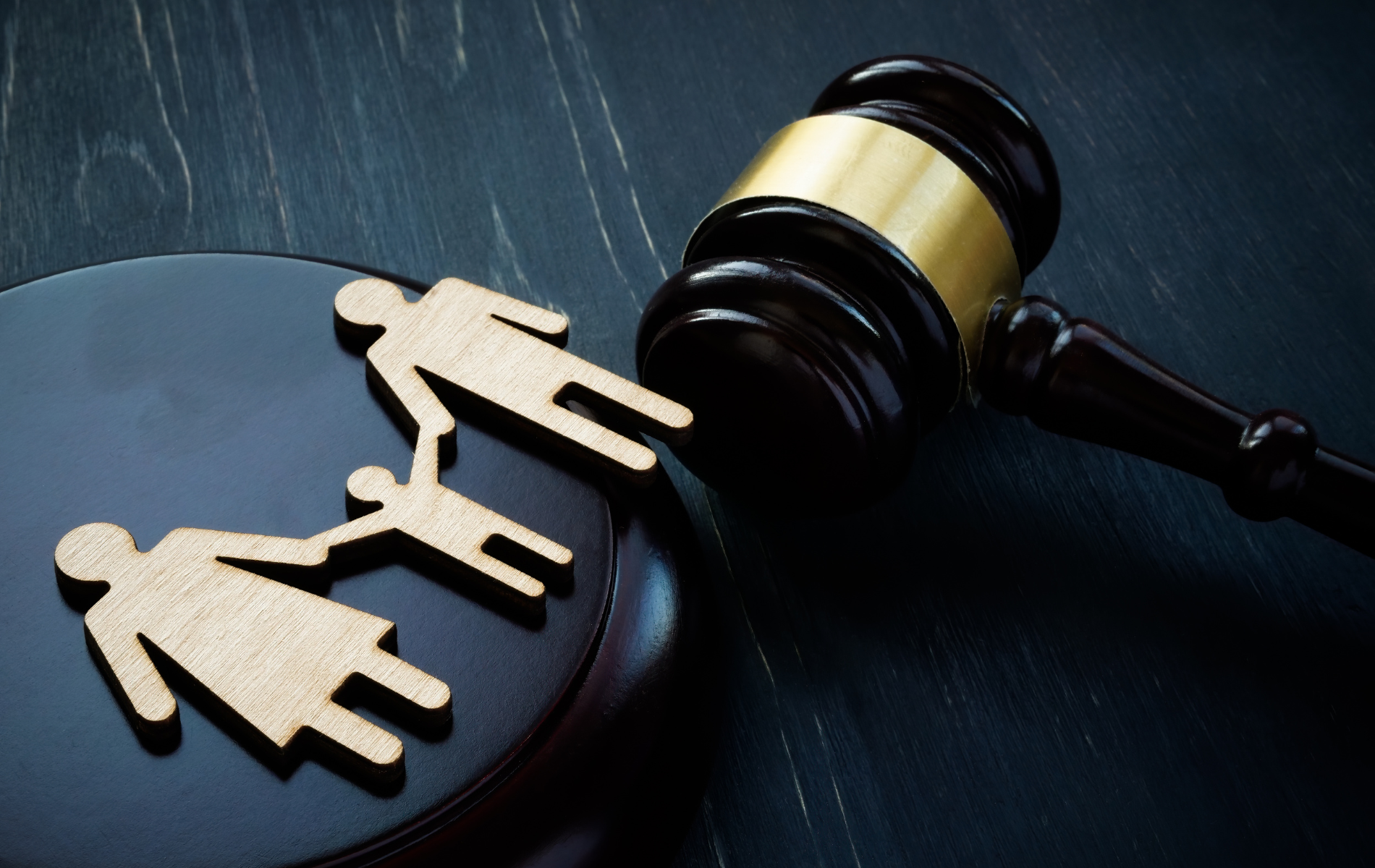 Wooden family figures split by gavel on a black surface, symbolizing family law or divorce.