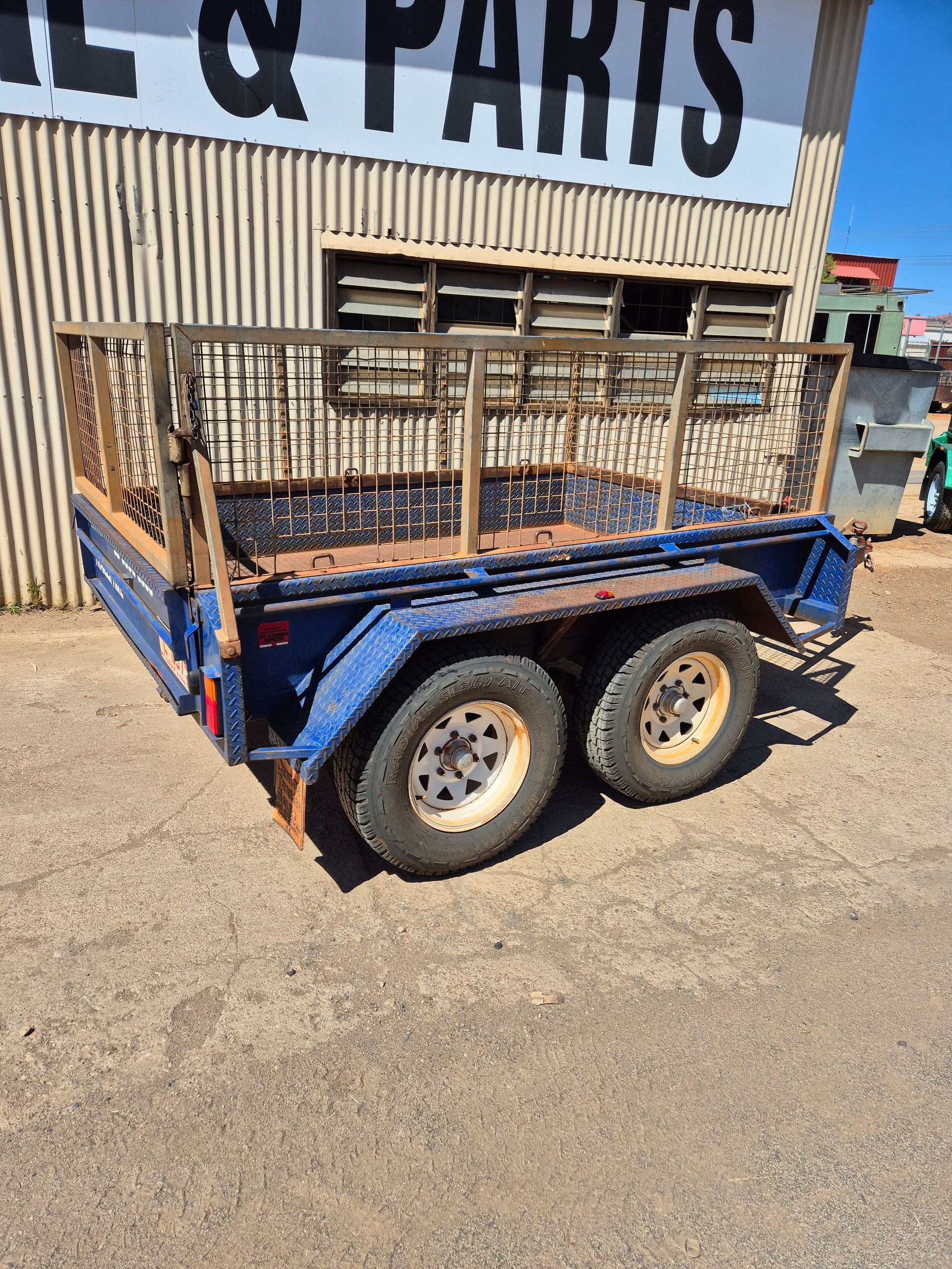 Blue Utility Trailer with Metal Cage Sides Parked on Pavement — Centre Trailer Sales In Alice Springs, NT