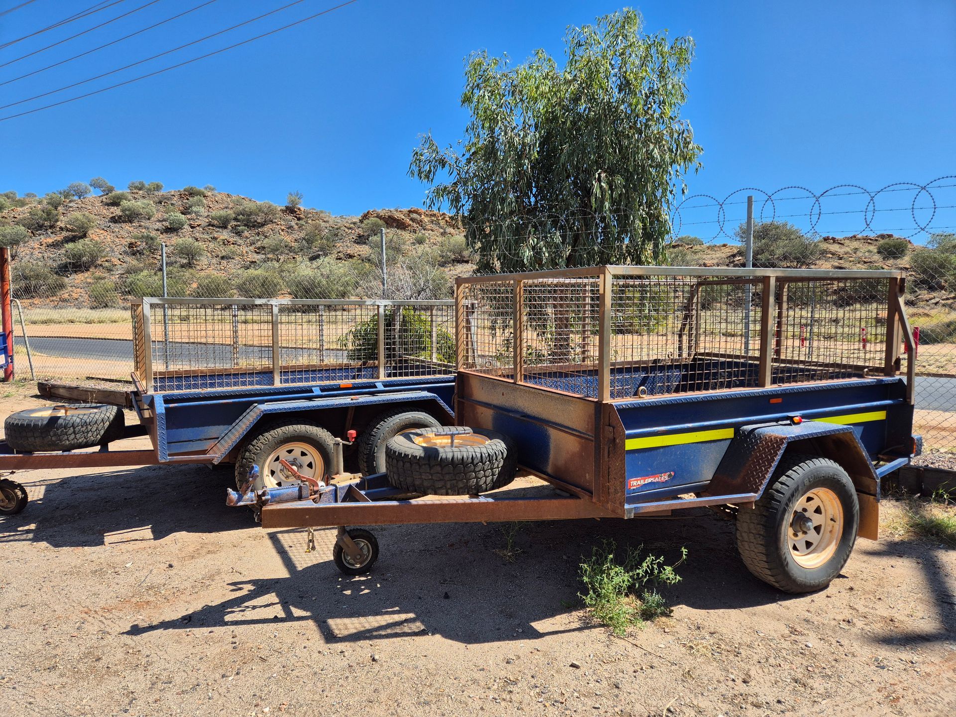 Two Blue Trailers with Metal Cages Parked on Dirt — Centre Trailer Sales In Alice Springs, NT
