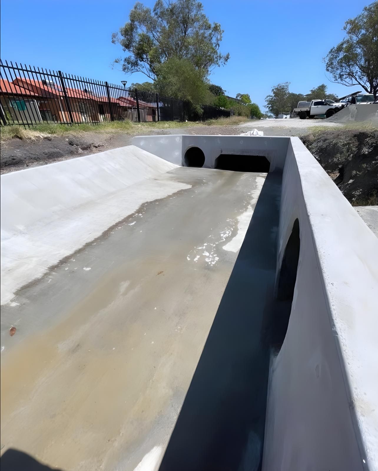 A Concrete Bridge Over a Muddy River With a Fence in the Background — Coastal Kerb and Concrete In Newcastle, NSW