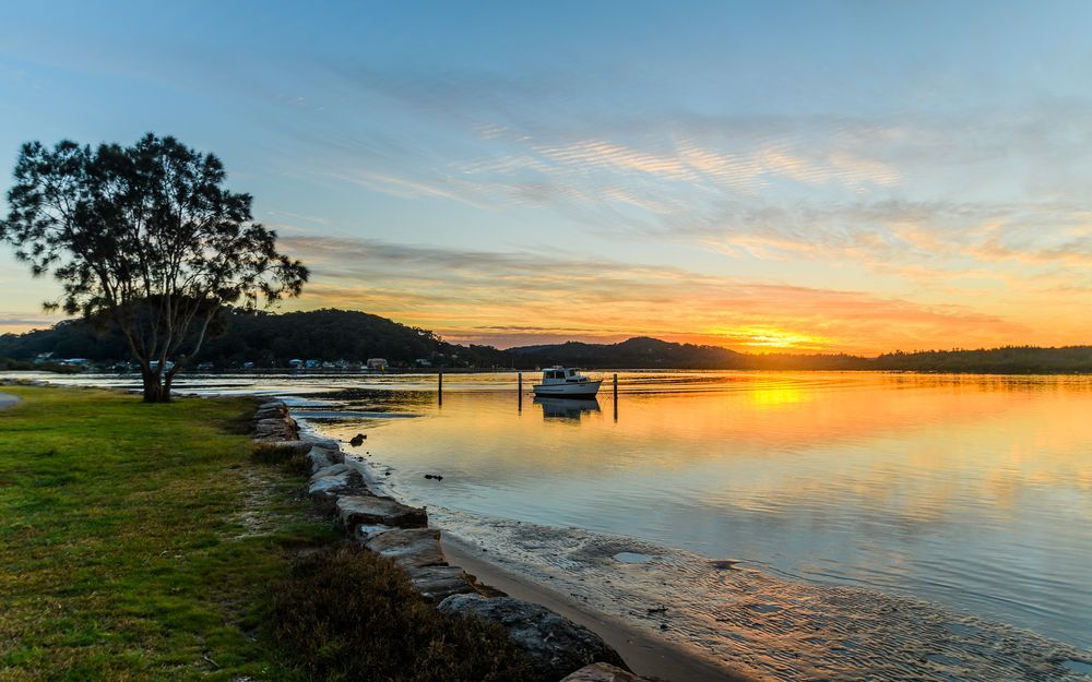 A Sunset Over a Body of Water With a Boat in the Water — Coastal Kerb and Concrete In Woy Woy, NSW