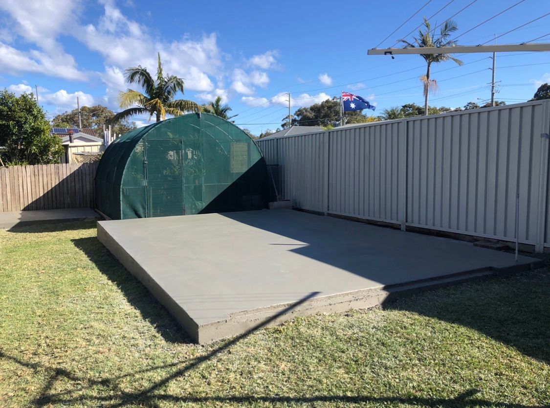 A Greenhouse is Behind a Fence in a Backyard — Coastal Kerb and Concrete In Woy Woy, NSW