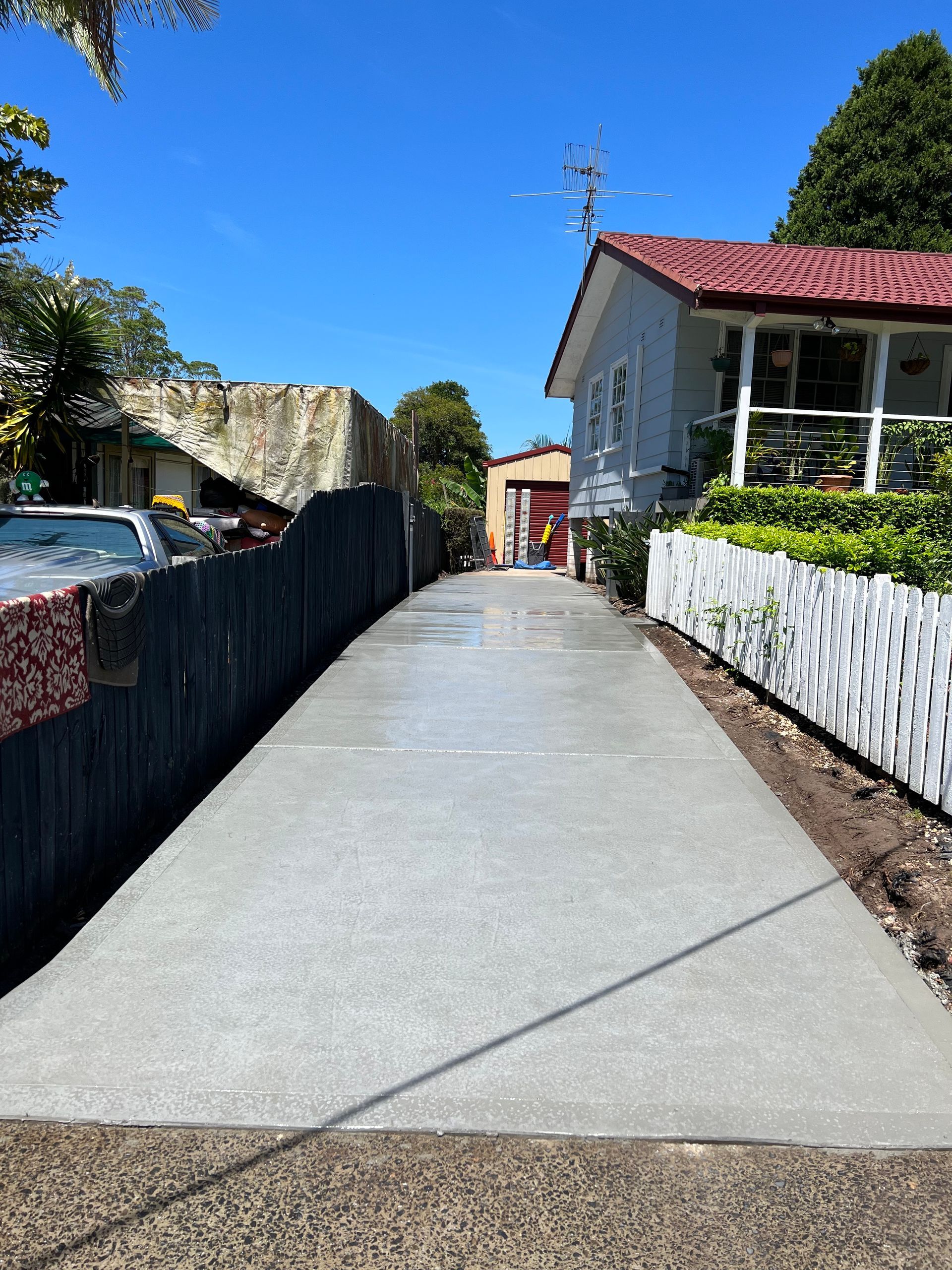 A Concrete Driveway Leading to a House With a Red Roof — Coastal Kerb and Concrete In Buff Point, NSW