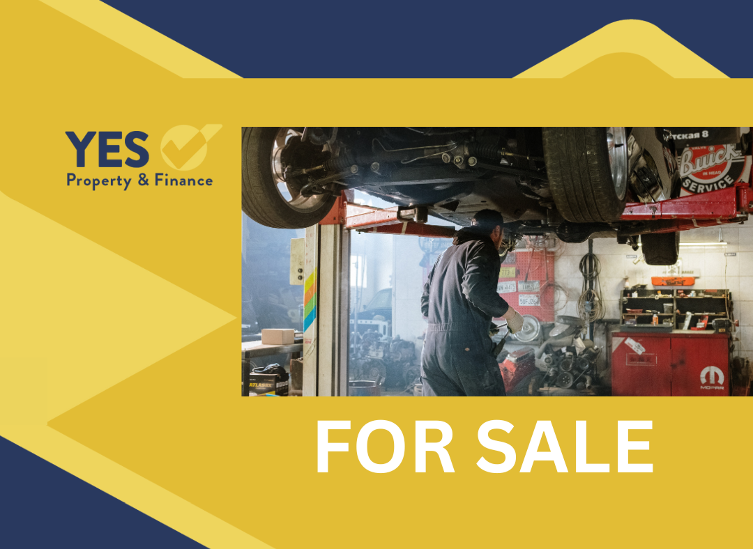 Mechanic working under a car in a shop. Sign reads