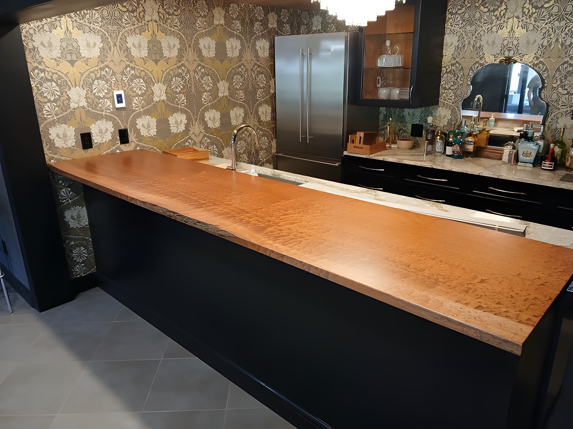 Modern kitchen with a long wooden island, black base, tiled backsplash, and stainless steel refrigerator.