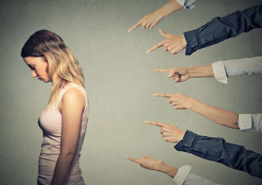 Uma mulher está parada na frente de um grupo de pessoas apontando para ela.