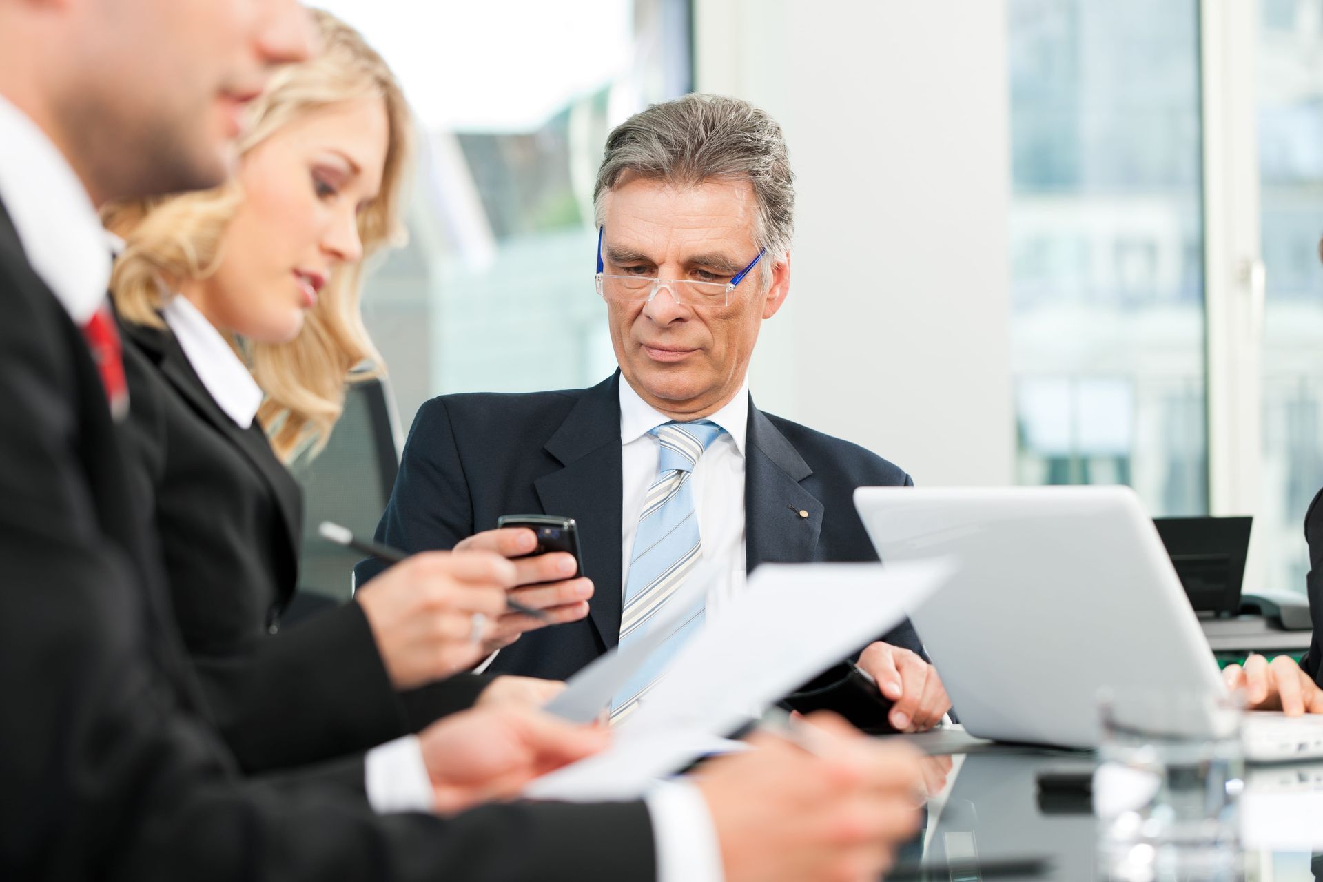 Um grupo de empresários está sentado à mesa com laptops e papéis.