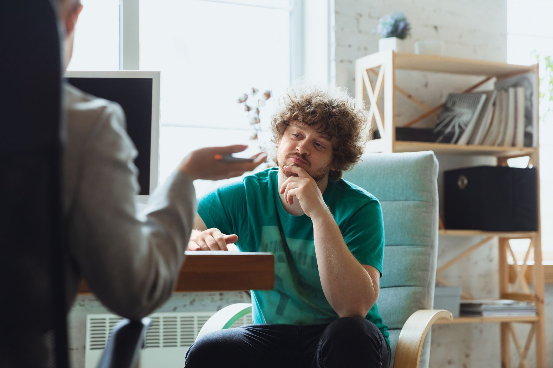 Um homem está sentado em uma cadeira conversando com outro homem.