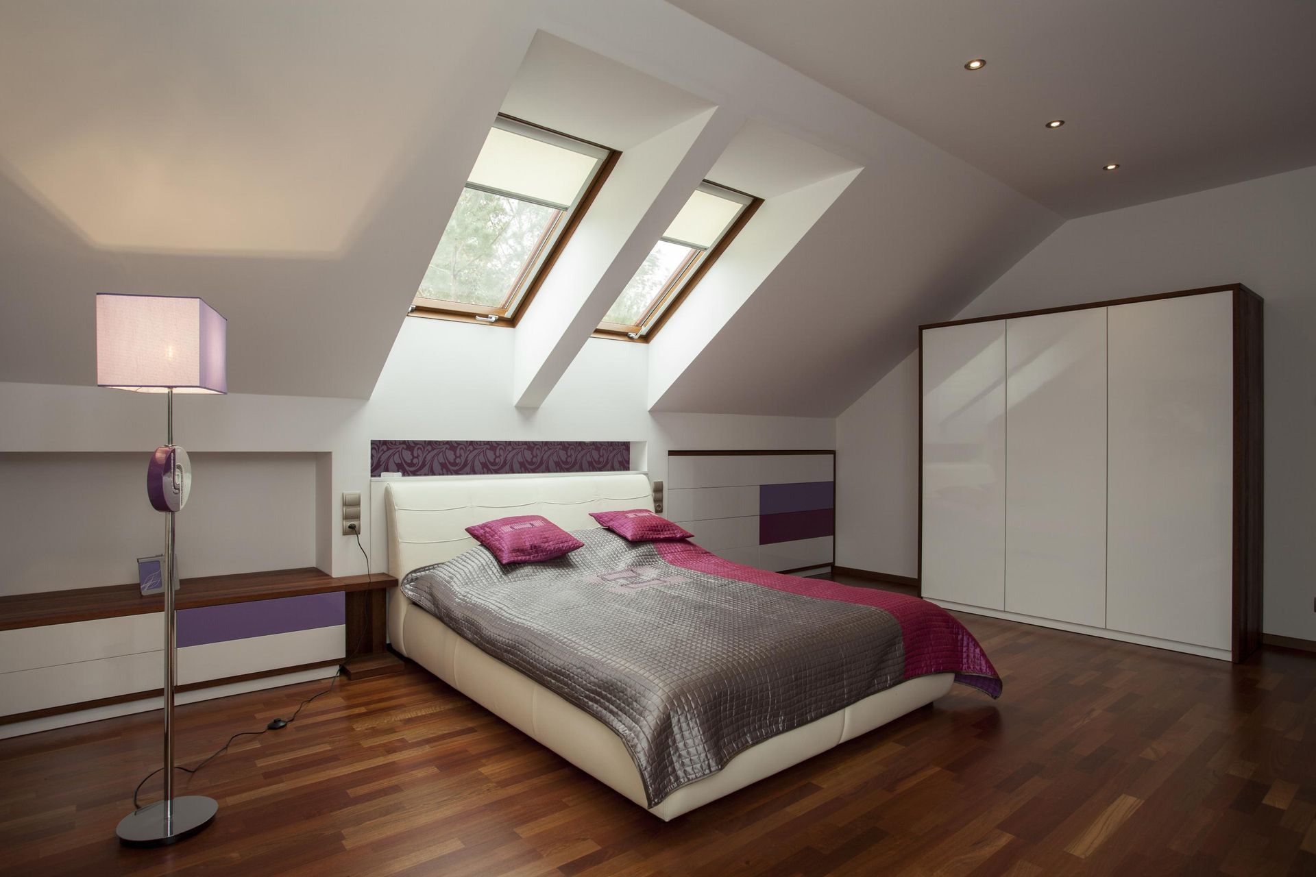 Spacious attic bedroom with a double bed, skylights, wooden floor, and a white wardrobe