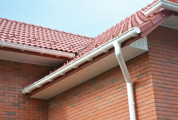 House roof with red tiles, white guttering, and a brick wall below