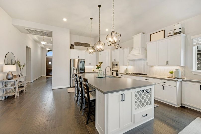 Bright modern white kitchen with island, bar stools, pendant lights, and hardwood floors