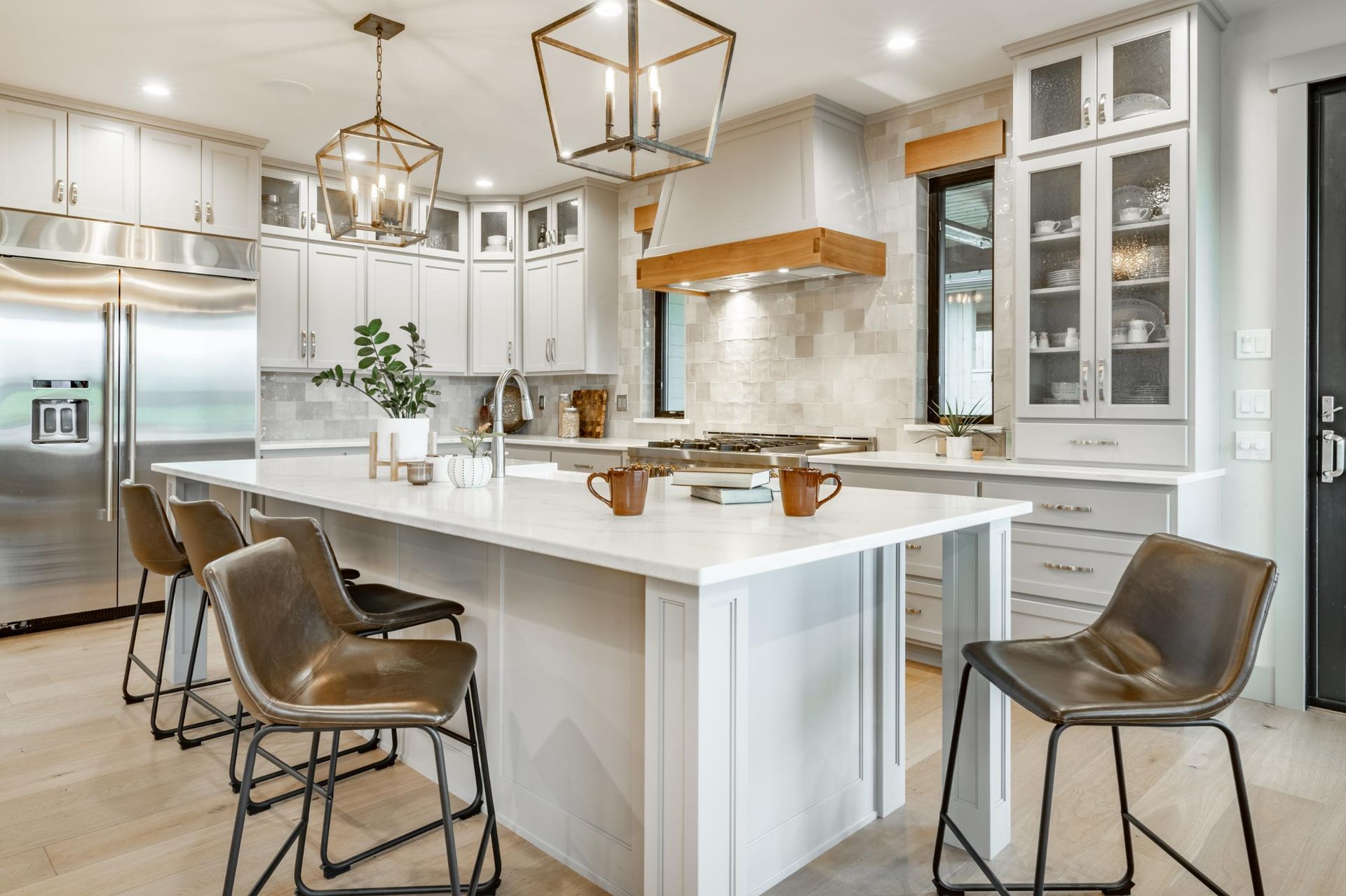 Bright modern white kitchen with marble island, pendant lights, bar stools, and stainless steel appliances