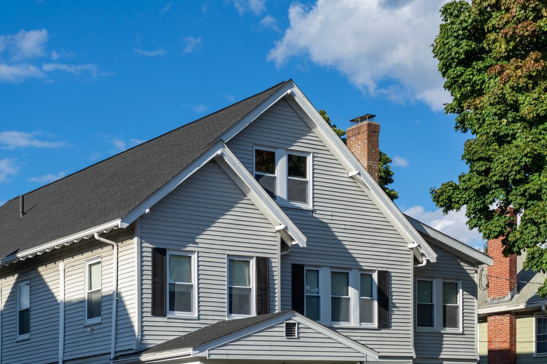 Gray house with black roof, white trim, and a brick chimney under a blue sky