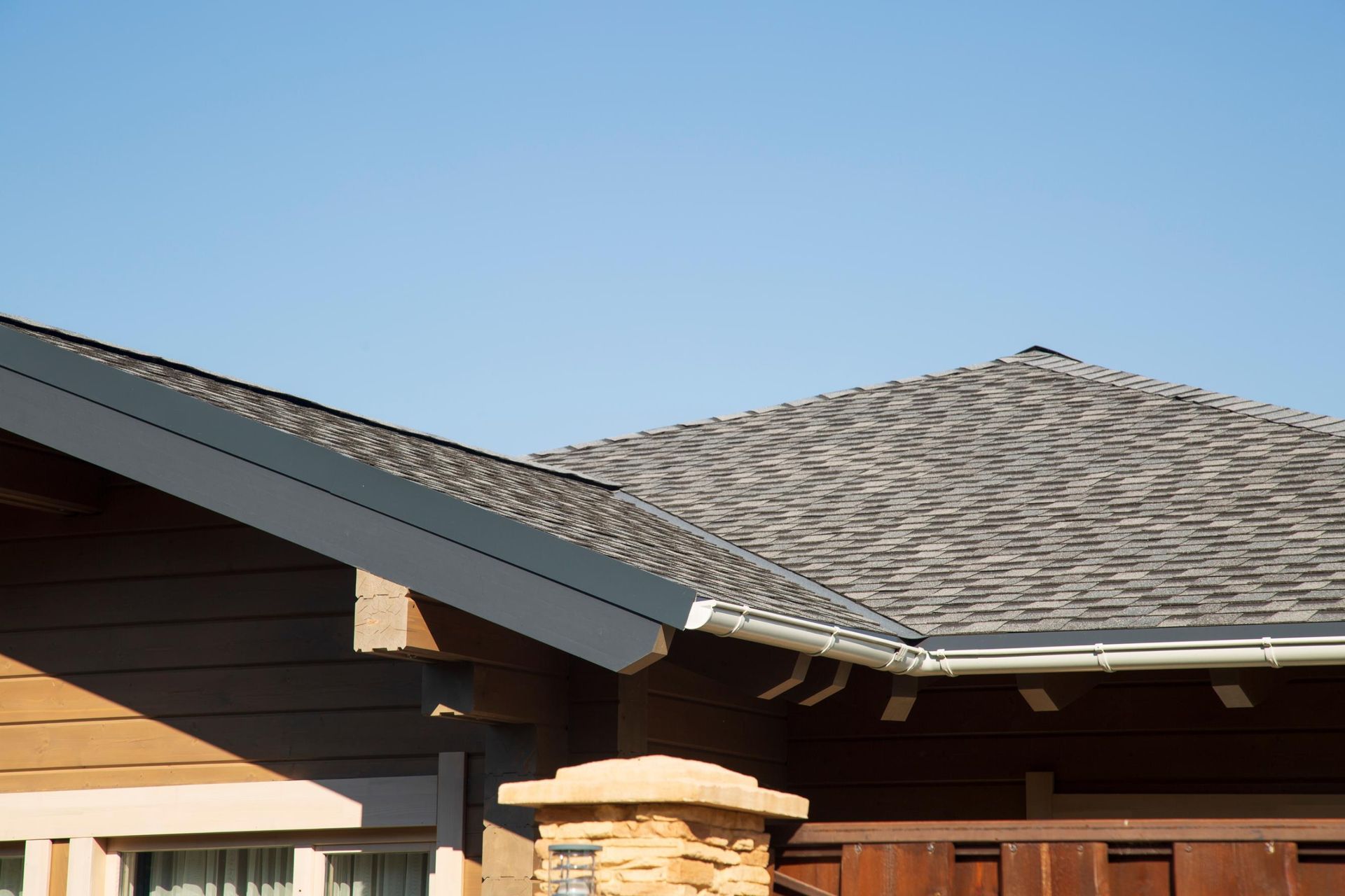 House roof with gray shingles and dark trim against a clear blue sky