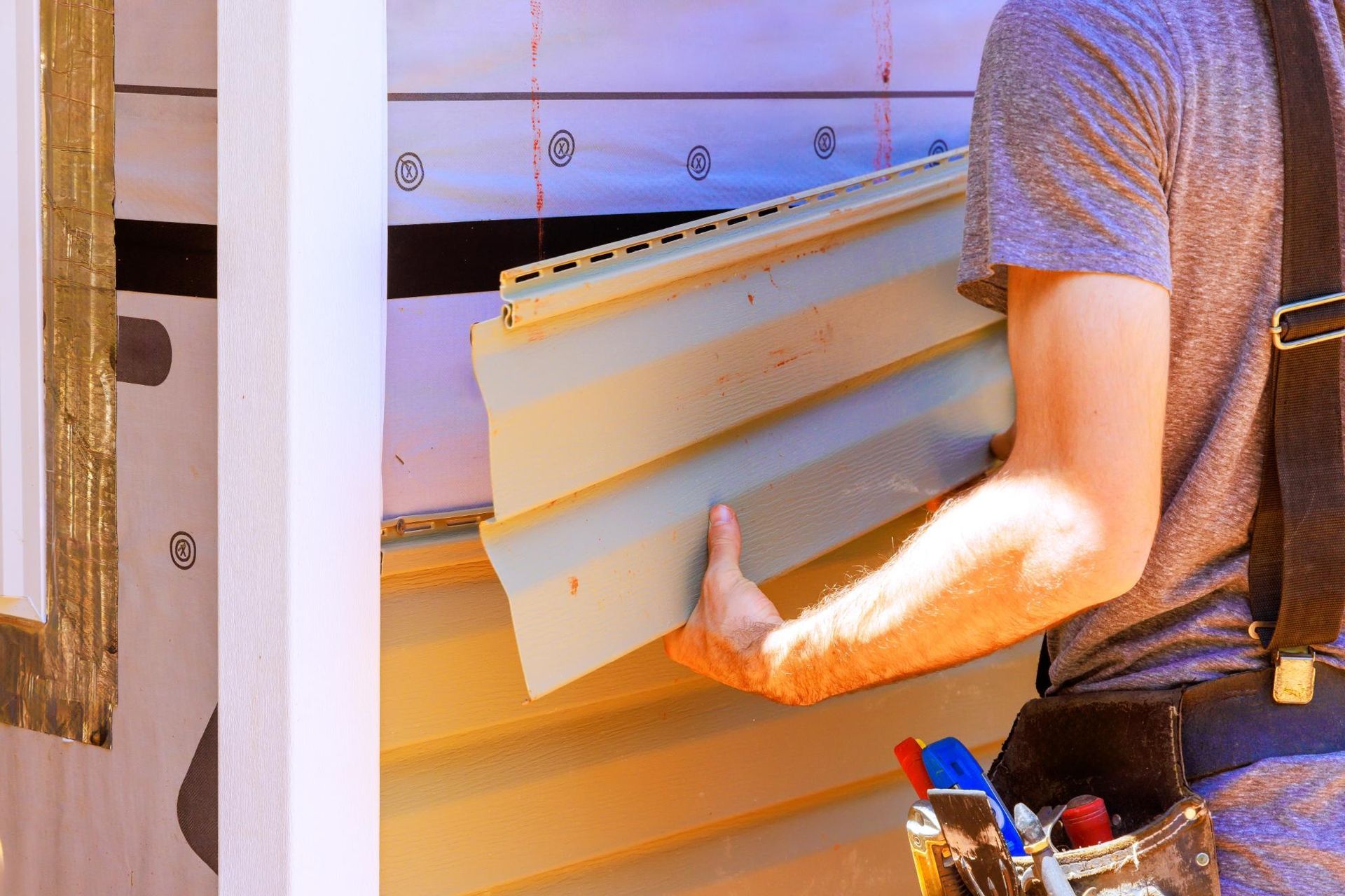Worker carrying white siding panels at a construction site