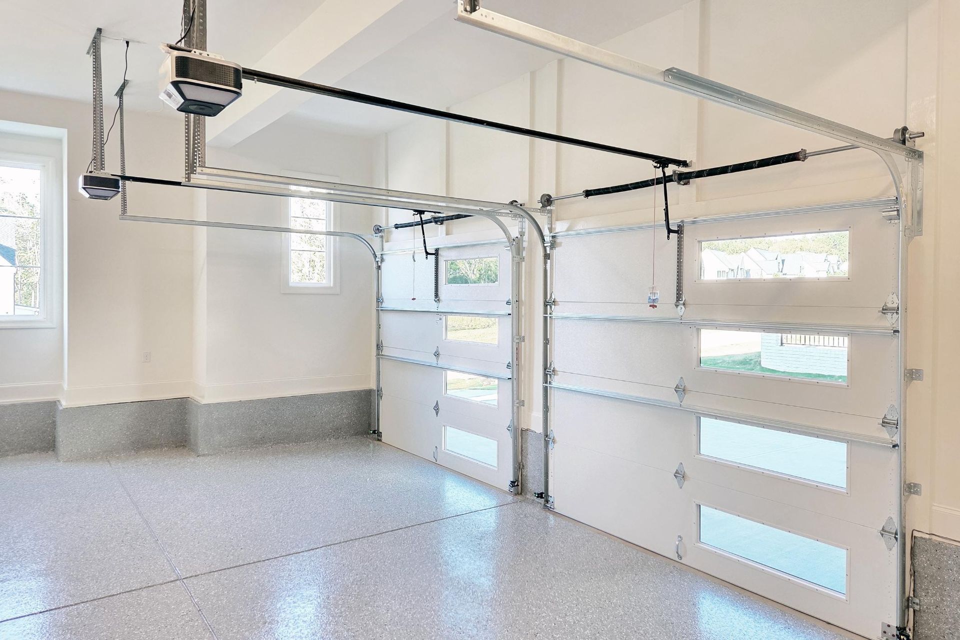 Empty two-car garage with white doors, windows, and speckled concrete floor.